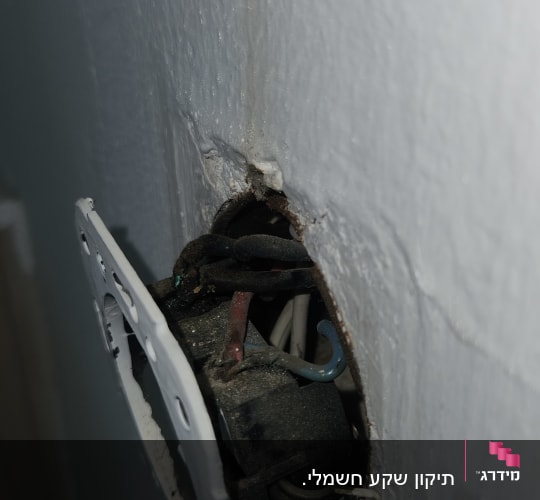 חוטי חשמל חשופים בקיר עם שקע פתוח
